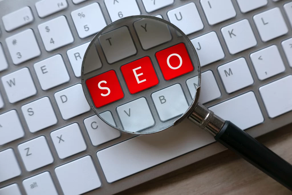 A magnifying glass focusing on the red keys spelling "SEO" on a keyboard, symbolizing search engine optimization services provided by a digital marketing agency in Dallas.