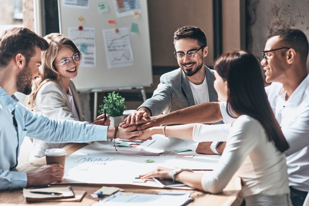 A group of enthusiastic professionals putting their hands together in a gesture of unity during a meeting about blog writing services.