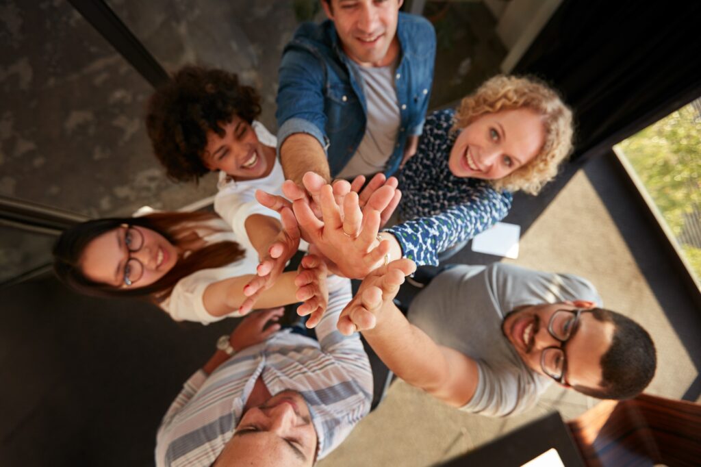 Group of diverse people in a team huddle, reaching out with their hands together, symbolizing teamwork in SEO services in Denver.