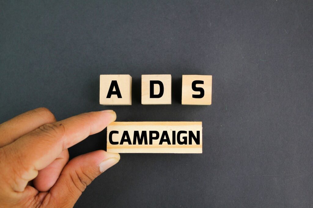 A hand arranging wooden blocks spelling out 'ADS CAMPAIGN' on a black background.