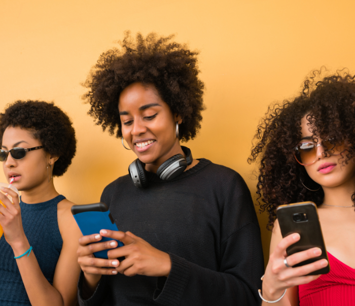 Three young women using smartphones against a yellow background – mobile-friendly design concept