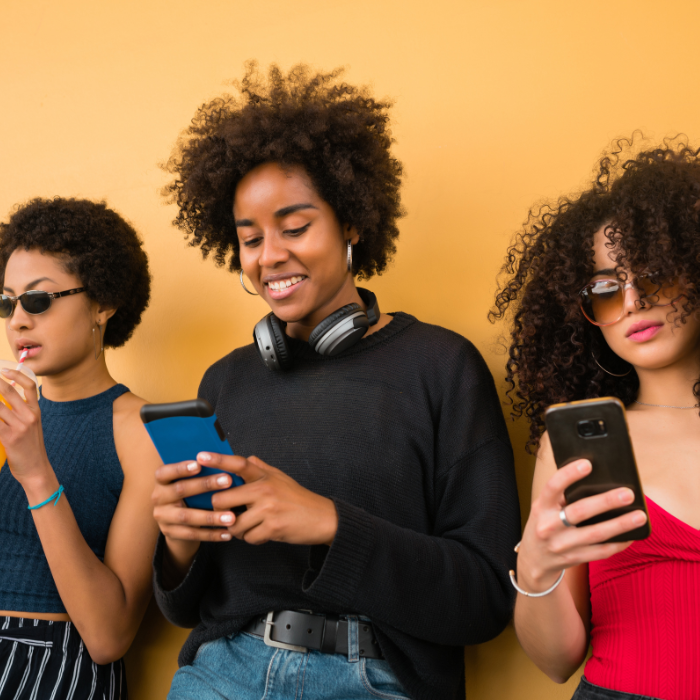 Three young women using smartphones against a yellow background – mobile-friendly design concept